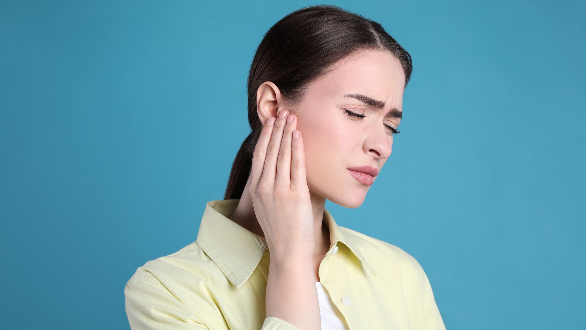 Mujer expresando dolor mientras sostiene su mano sobre su oreja derecha.