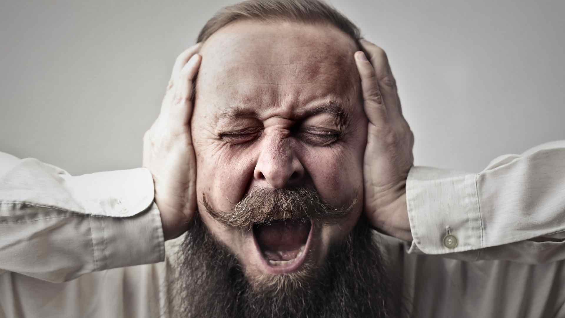 A man holding his ear and looking stressed out.